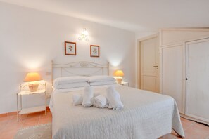 Cama bem arrumada com lençóis e toalhas brancos, duas luminárias de cabeceira e quadros nas paredes.