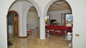 A spacious dining area with a red table and chairs, white walls, and a view of the outdoors. - Villa Nice Mondello  (Palermo)