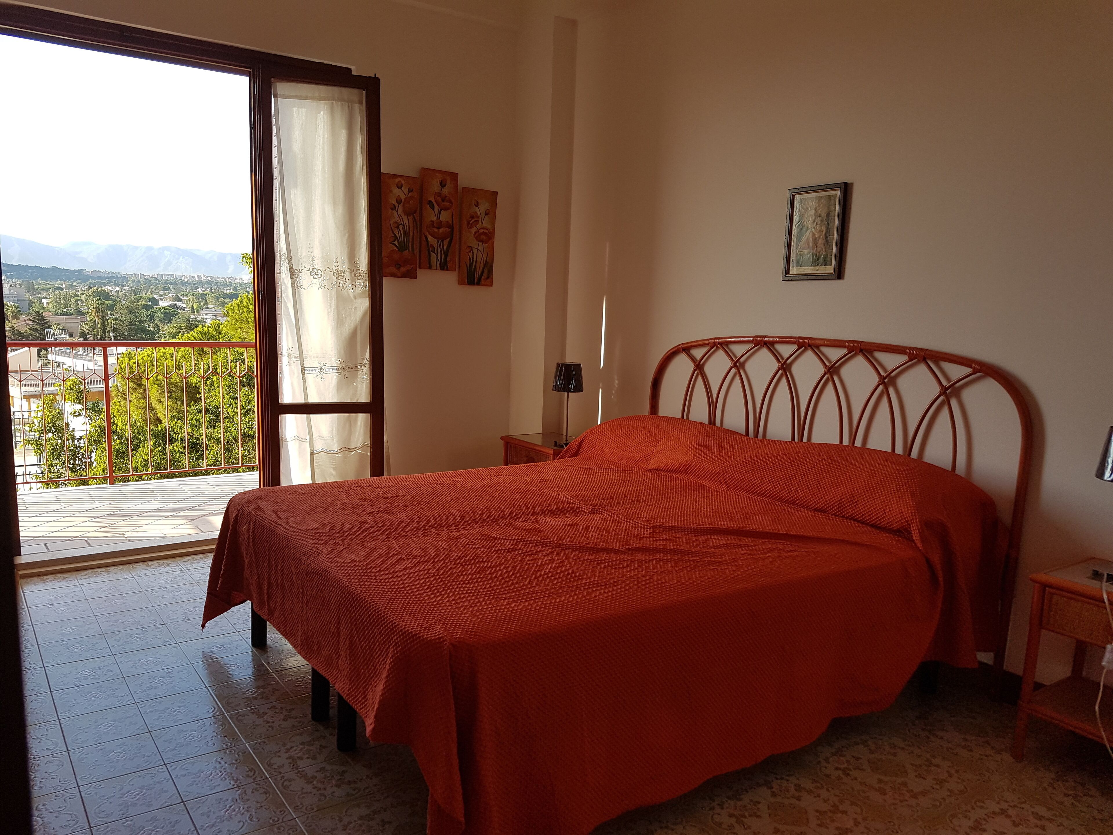 Une chambre à coucher comprenant un lit, une table de chevet, une lampe et donnant sur un balcon avec une balustrade.
