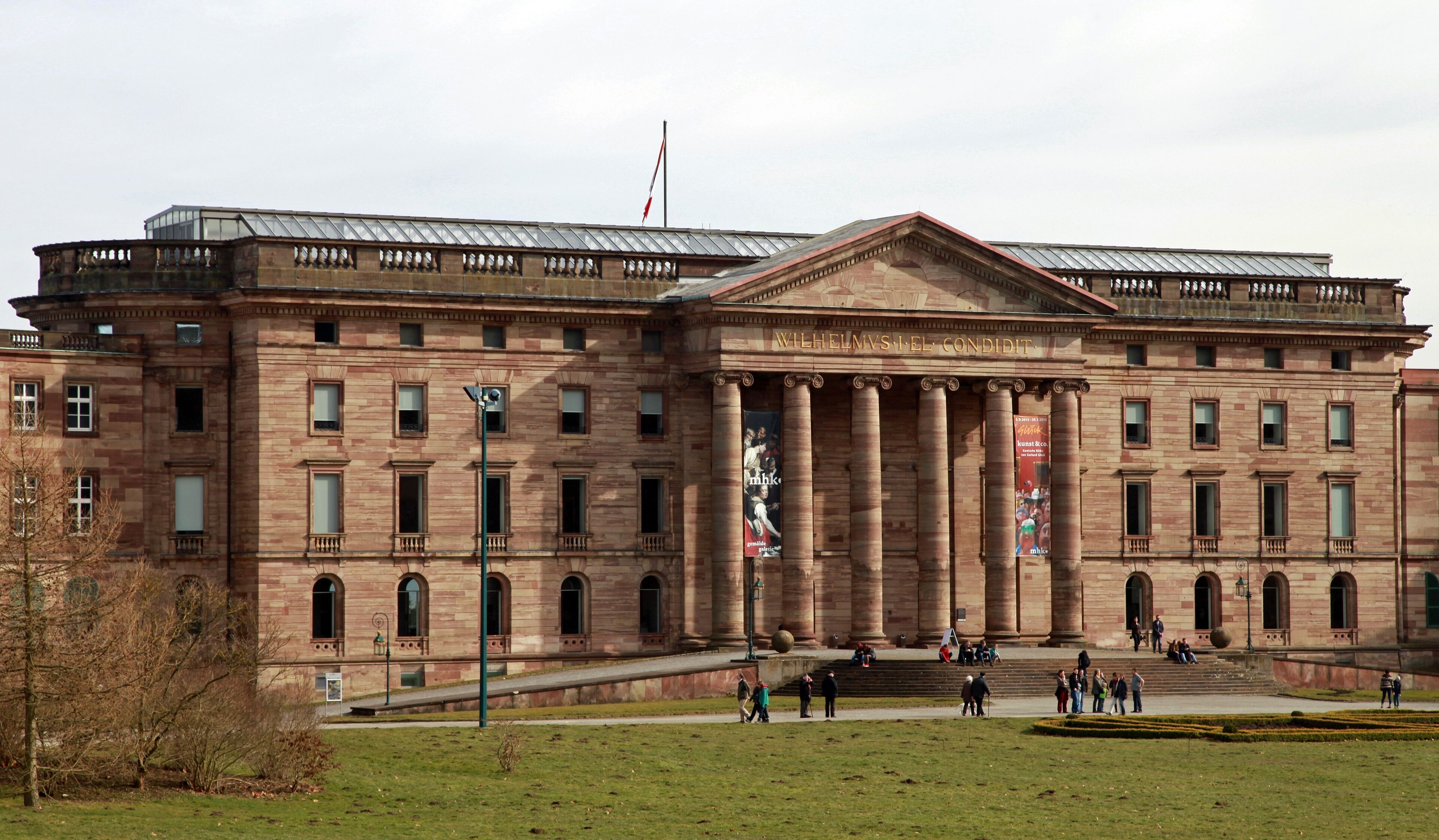 A large, historic building with classical architecture, featuring a prominent entrance with columns and a central pediment.