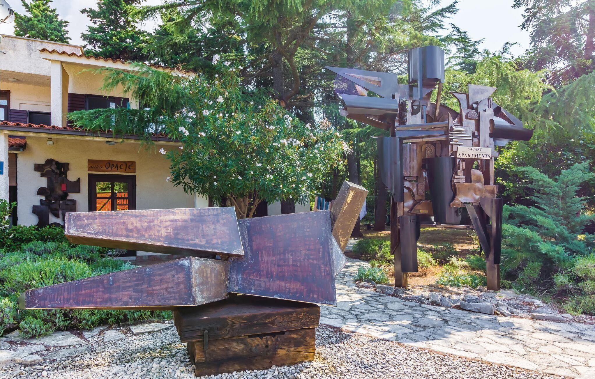 Une sculpture métallique dans un jardin, avec un bâtiment en arrière-plan.