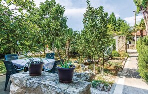 Une terrasse avec une table et des chaises, entourée de plantes en pot et d’arbres.