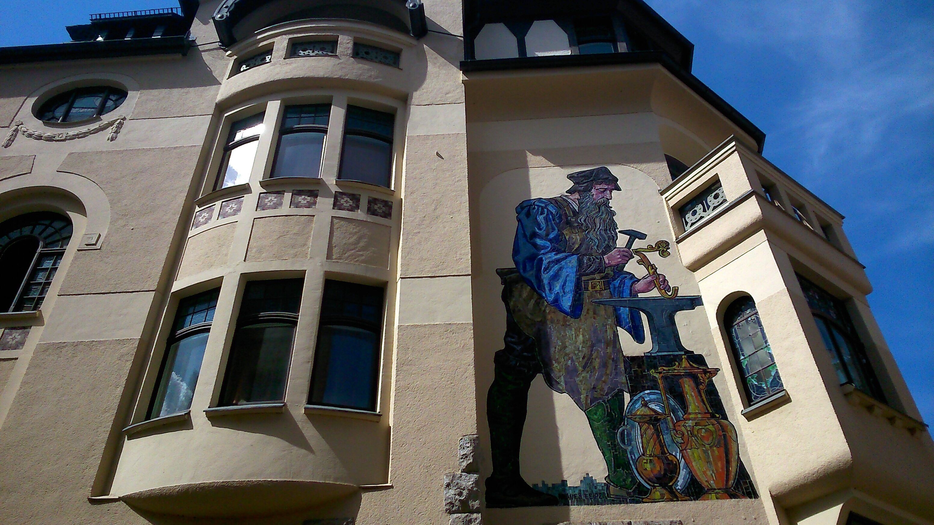 Ein Gebäude mit einem Eckturm, großen Fenstern und einem Wandbild einer Person, die einen Hammer und eine Meißel hält.