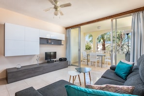 A modern living room with a sofa, TV, and a balcony with outdoor furniture.