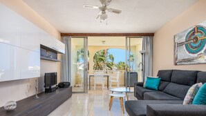 A modern living room with a sofa, TV, and a balcony with a view of palm trees. - Family-friendly apartment 4 people. near sea and pool (Callao Salvaje)