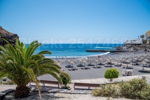 Una playa con sillas de playa y sombrillas, un acantilado rocoso y el océano.