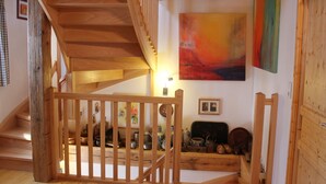 A wooden staircase with a railing, a painting on the wall, and a shelf with various items. - Charming Cottage La Maisonnette Coquette (Oltingue)