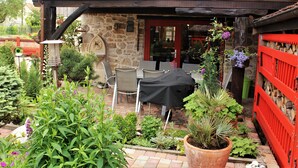 An outdoor patio with a table and chairs, surrounded by potted plants and a red fence. - Charming Cottage La Maisonnette Coquette (Oltingue)