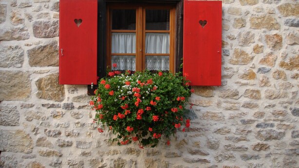 A stone building with a window featuring red shutters and a hanging flower basket. - Charming Cottage La Maisonnette Coquette (Oltingue)