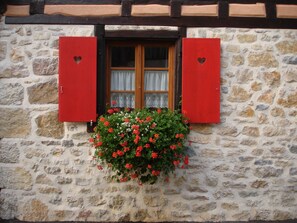 A stone building with a window featuring red shutters and a hanging flower basket.