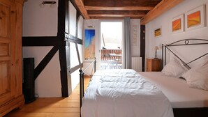 A bedroom with a bed, wooden beams, a balcony, and a view of the outside. - Charming Cottage La Maisonnette Coquette (Oltingue)