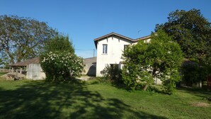 A two-story house with a white facade, a tiled roof, and a small garden area with trees and a lawn. - quiet house on the banks of the Dordogne near Saint Emilion (Sainte-Terre)