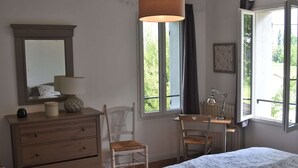 A bedroom with a bed, a dresser, a chair, a desk, a lamp, and a window with a view of greenery. - quiet house on the banks of the Dordogne near Saint Emilion (Sainte-Terre)