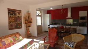 A living room with a colorful sofa, a wooden chair, and a wicker chair with a checkered cushion. A kitchen with red walls, a white refrigerator, and a double oven is visible. - quiet house on the banks of the Dordogne near Saint Emilion (Sainte-Terre)