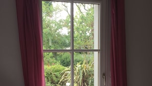 Ein Zimmer mit Bett, einem fenster mit Vorhängen und Blick auf einen Garten.