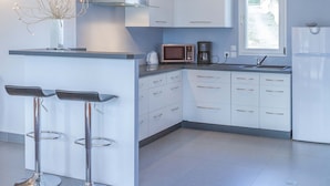 Eine moderne Küche mit weißen Schränken, einer zentralen Kochinsel mit Barhocker, einer Mikrowelle, einer Kaffeemaschine und einem eingebauten Backofen.