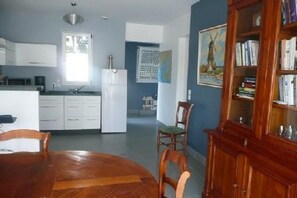 A modern kitchen with white cabinets, a dining table with chairs, and a wooden bookcase.