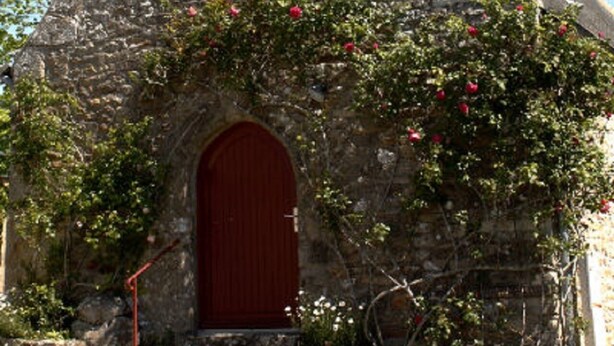 Eine Steinkirche mit roter Tür und Kruzifix.