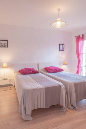 A bedroom with two beds, each with a pink pillow, a bedside lamp, and a hanging light fixture.