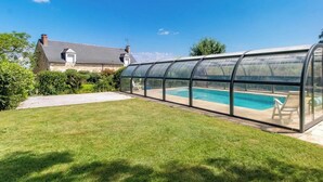En swimmingpool med en glasvägg runt om, en gräsyta och ett stenhus i bakgrunden.