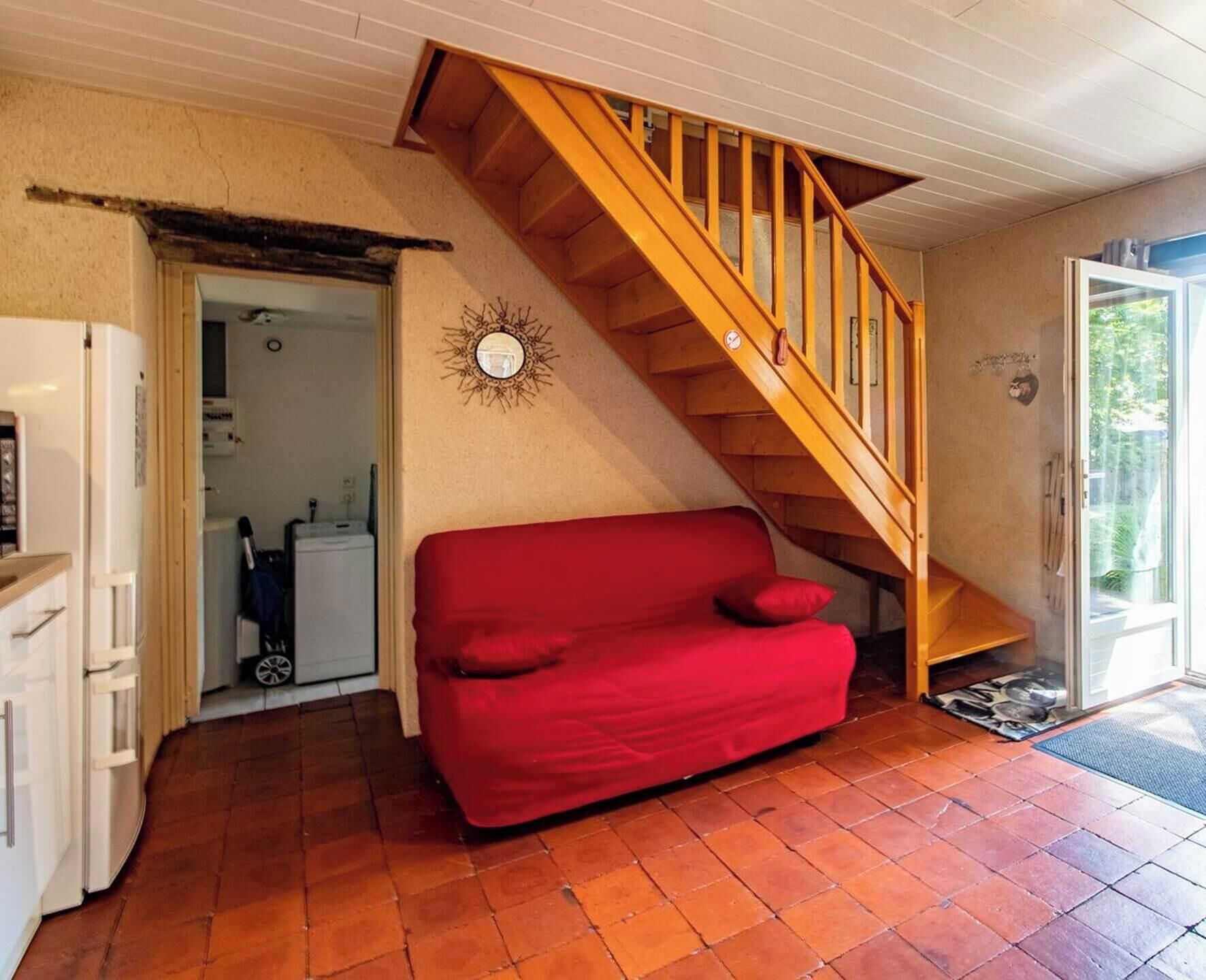 En kompakt opholdsstue med en rød sofa, en trætrappe og et hvidt køleskab.
