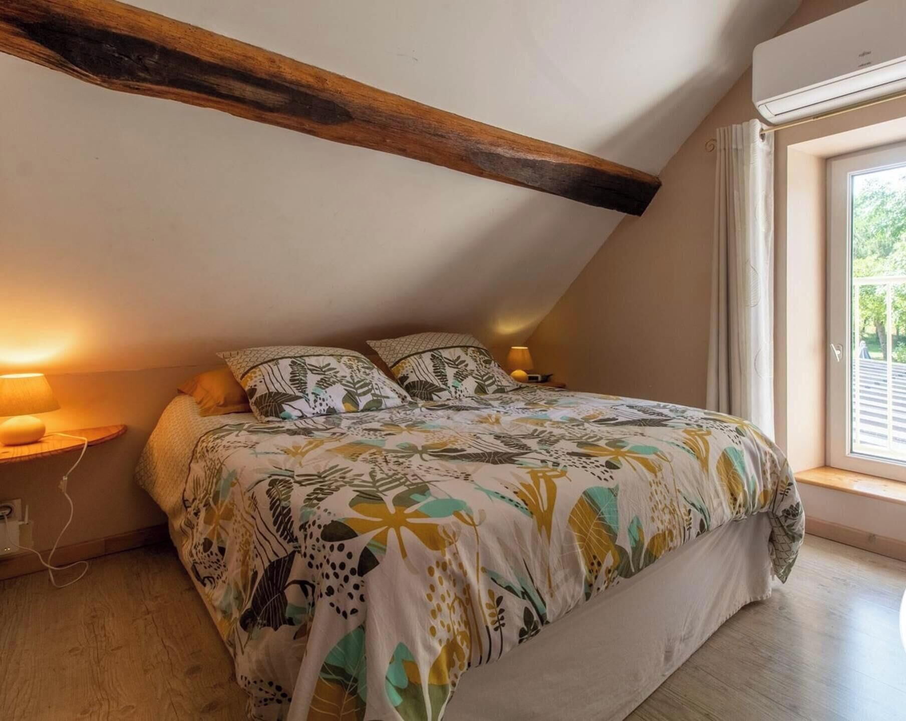 Un dormitorio con techo inclinado, cama con ropa de cama estampada, lámparas de noche y ventana con vistas.