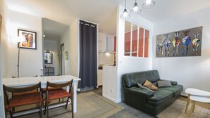 Een moderne woonkamer met een groene bank, een eettafel met stoelen, en een keuken op de achtergrond.