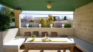 Un espace extérieur abrité, aménagé avec une table, des coussins et une plante en pot.