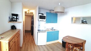 Cocina compacta con armarios de madera, microondas, refrigerador pequeño y un comedor con taburetes.