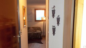 Un pasillo estrecho con suelo de madera, una cama al fondo y lámparas fijadas a la pared.
