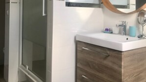 A bathroom with a glass shower enclosure, a wooden vanity with a mirror, and a white sink.
