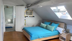 A bedroom with a wooden bed, a skylight, a bedside table, and a door leading to another room.