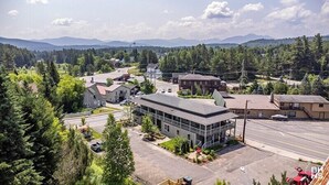 Une petite ville où se côtoient des bâtiments résidentiels et commerciaux, entourée de forêts denses et dominée par des montagnes en arrière-plan.