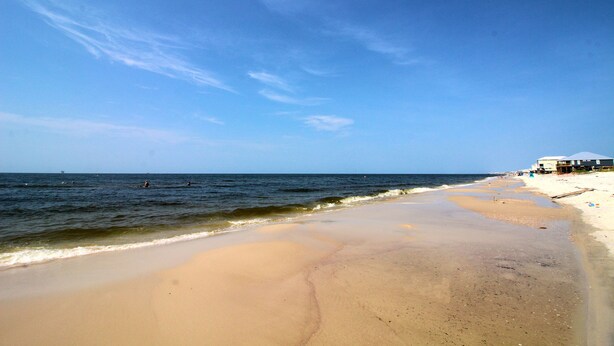 Una playa con cielo despejado, mar tranquilo y un edificio a la derecha.