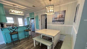 Una cocina con una mesa de madera, dos taburetes altos y una lámpara colgante.