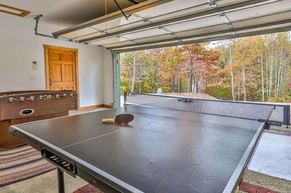 Ein Pingpongtisch mit Netz, eine Holztür und Blick auf Herbstbäume durch ein großes Fenster.