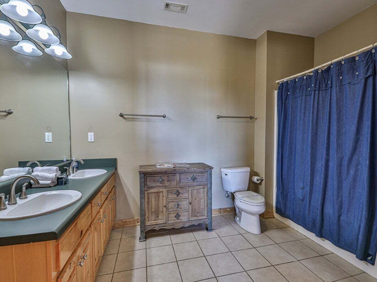 Une salle de bain avec deux lavabos, un meuble en bois, des toilettes et un rideau de douche.