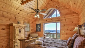 Un dormitorio de cabaña acogedor con una cama grande, un aparador de madera, un escritorio y vistas al exterior.