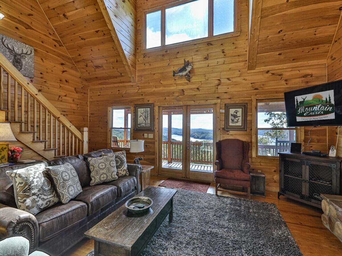 Ein Holzblockhaus im Inneren mit einer Couch, einem Sessel und einem Fernseher an der Wand.