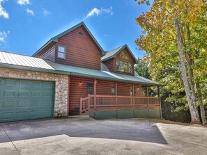 A log cabin with a stone foundation, a green garage door, and a porch with a railing. - Home Run View by Mountain Oasis | Carters Lake & Mountain Views (Ellijay)