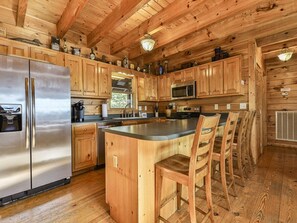A wooden cabin-style kitchen with a stainless steel refrigerator, wooden cabinets, a microwave, and a bar area with wooden chairs. - Home Run View by Mountain Oasis | Carters Lake & Mountain Views (Ellijay)
