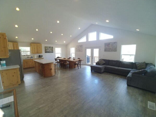 A spacious living area with a large gray sofa, wooden dining table, and a kitchen with wooden cabinets.