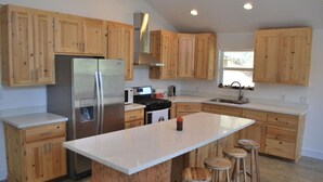 Una cocina moderna con armarios de madera, un refrigerador de acero inoxidable, una isla central con taburetes y un ventanal que proporciona luz natural.