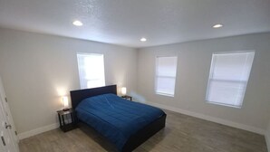 Un dormitorio con una cama, dos mesitas de noche y tres ventanas.