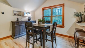 A dining area with a wooden table, chairs, a cabinet, and a window with a view of trees. - Close-Country Retreat (Eugene)