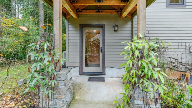 A wooden porch with a stone step leading to a gray door, surrounded by greenery. - Close-Country Retreat (Eugene)