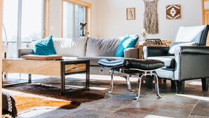 A spacious living room with a high ceiling, large windows, a wooden ceiling, a sofa, a coffee table, and a fireplace.