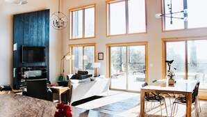 A spacious living area with a large TV, wooden furniture, and multiple windows providing natural light.