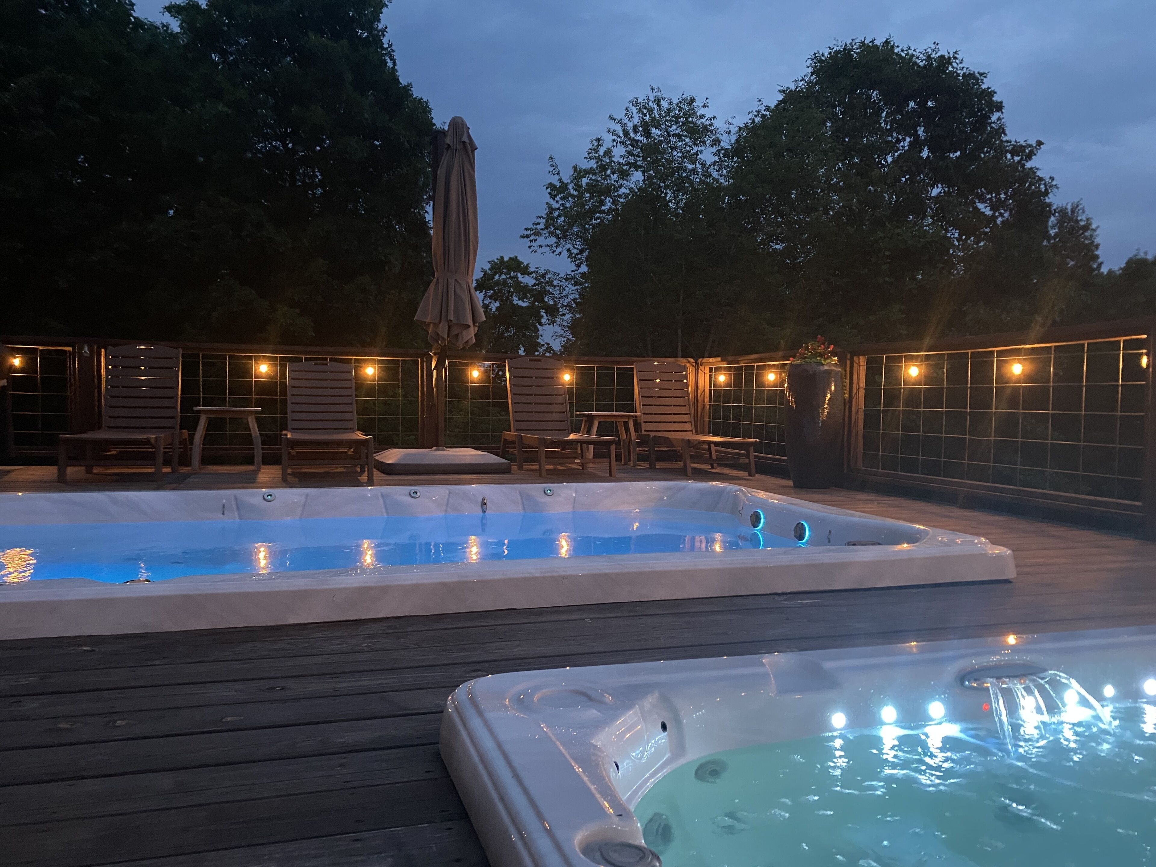 Ett område med ett bubbelbad, en träaltan, solstolar och ljusslingor.