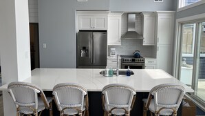 A modern kitchen with white cabinetry, a stainless steel refrigerator, a gas stove, and a large island with bar stools. - 4 Br, 2 Ba Penthouse Condo with Ocean View- Beach Block- Heart of Sea Isle City (Sea Isle City)
